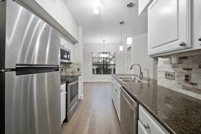 kitchen with sink, appliances with stainless steel finishes, white cabinetry, hanging light fixtures, and dark stone countertops