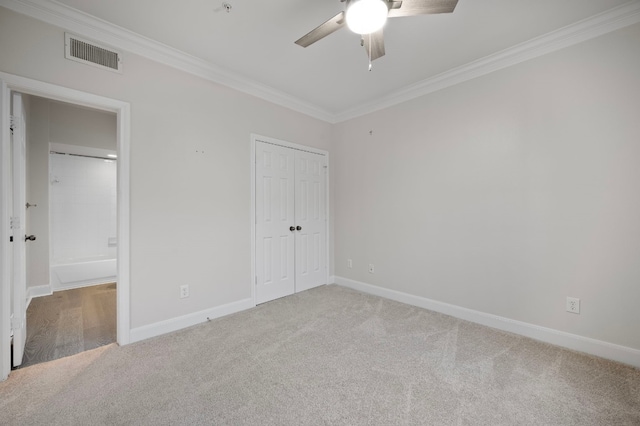 unfurnished bedroom featuring carpet flooring, ceiling fan, crown molding, ensuite bath, and a closet