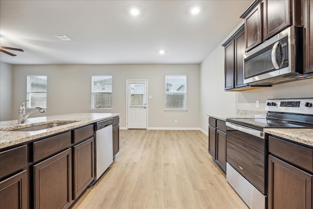 kitchen with dark brown cabinetry, appliances with stainless steel finishes, light stone countertops, and sink