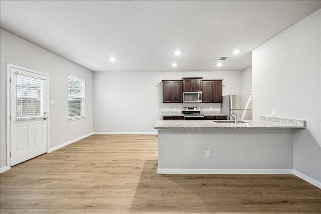 kitchen with sink, light stone counters, appliances with stainless steel finishes, kitchen peninsula, and light hardwood / wood-style floors