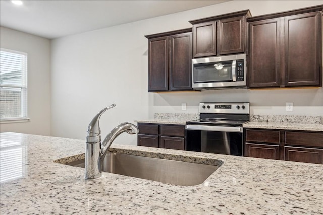 kitchen featuring stainless steel appliances, light stone countertops, sink, and dark brown cabinetry