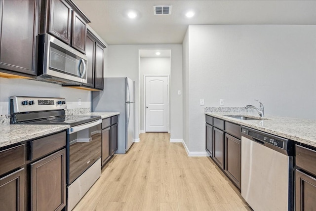 kitchen with appliances with stainless steel finishes, sink, dark brown cabinetry, light stone countertops, and light wood-type flooring