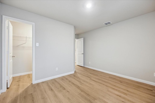 unfurnished bedroom featuring a spacious closet, light wood-type flooring, and a closet