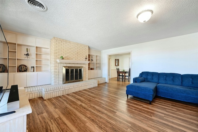 living room featuring a brick fireplace, hardwood / wood-style floors, a textured ceiling, and built in shelves