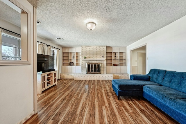 living room featuring dark hardwood / wood-style floors, a textured ceiling, a fireplace, and built in shelves