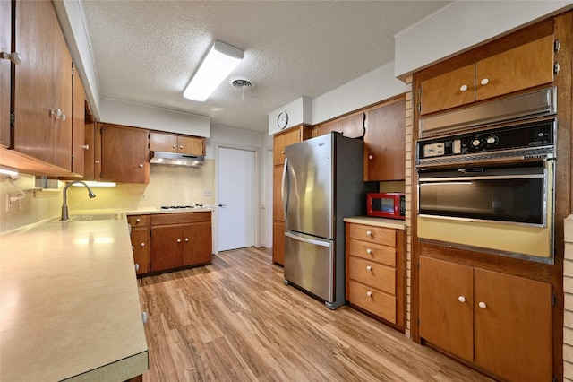 kitchen featuring sink, stainless steel fridge, wall oven, a textured ceiling, and light wood-type flooring