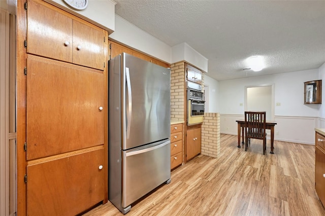 kitchen with stainless steel refrigerator, oven, a textured ceiling, and light wood-type flooring