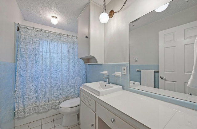 bathroom with tile walls, vanity, toilet, tile patterned floors, and a textured ceiling