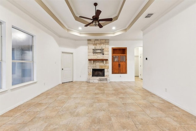 unfurnished living room featuring crown molding, a tray ceiling, a stone fireplace, and ceiling fan