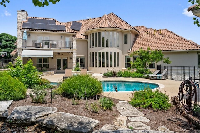 rear view of property featuring french doors, a balcony, a patio area, and solar panels