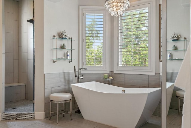 bathroom featuring independent shower and bath, a chandelier, a wealth of natural light, and tile walls