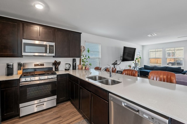 kitchen with sink, dark brown cabinets, appliances with stainless steel finishes, kitchen peninsula, and hardwood / wood-style flooring