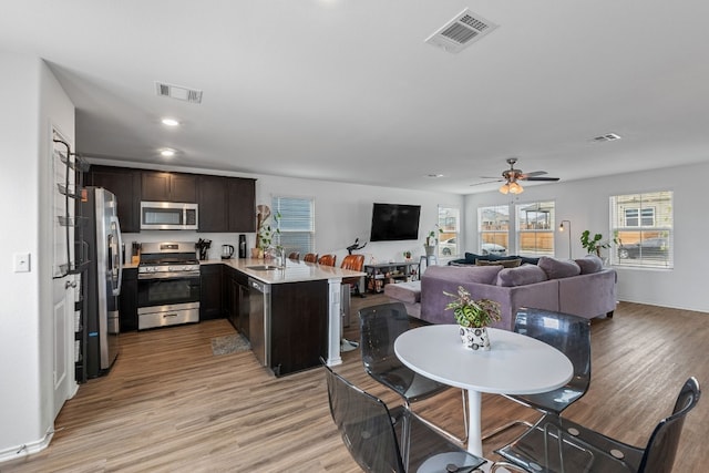 kitchen featuring sink, dark brown cabinetry, kitchen peninsula, stainless steel appliances, and light wood-type flooring