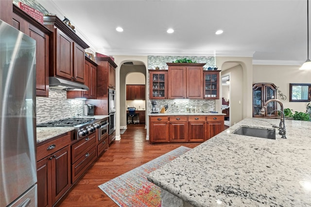 804 Laughing Dog Ct, Leander, TX 78641 - kitchen with arched walkways, stainless steel appliances, a sink, under cabinet range hood, and ornamental molding