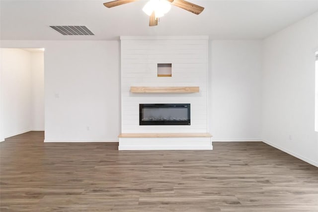 unfurnished living room with ceiling fan, a large fireplace, and dark hardwood / wood-style flooring