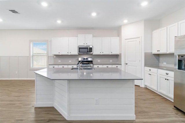 kitchen with a kitchen island with sink, stainless steel appliances, and white cabinets