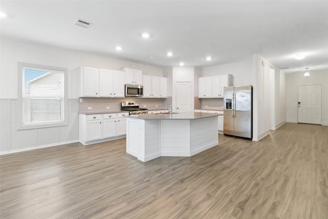 kitchen with appliances with stainless steel finishes, white cabinetry, sink, a kitchen island with sink, and light hardwood / wood-style floors