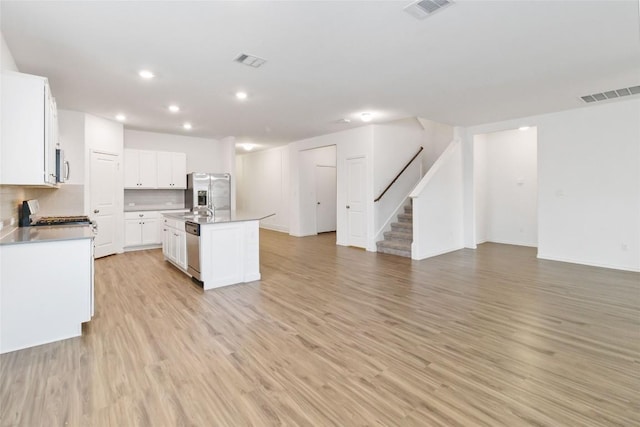 kitchen with white cabinets, decorative backsplash, stainless steel appliances, a center island with sink, and light wood-type flooring