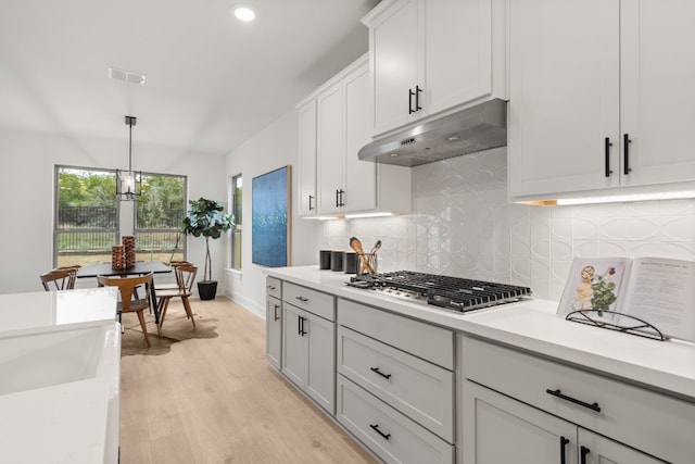 kitchen featuring pendant lighting, backsplash, light hardwood / wood-style floors, stainless steel gas cooktop, and white cabinets