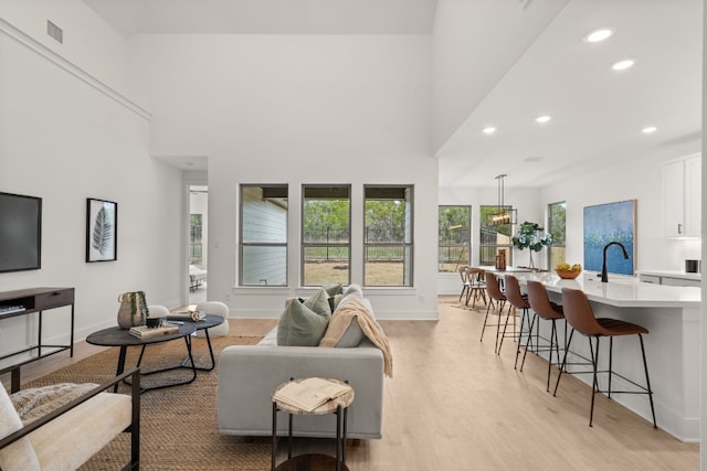 living room with a high ceiling, sink, and light wood-type flooring