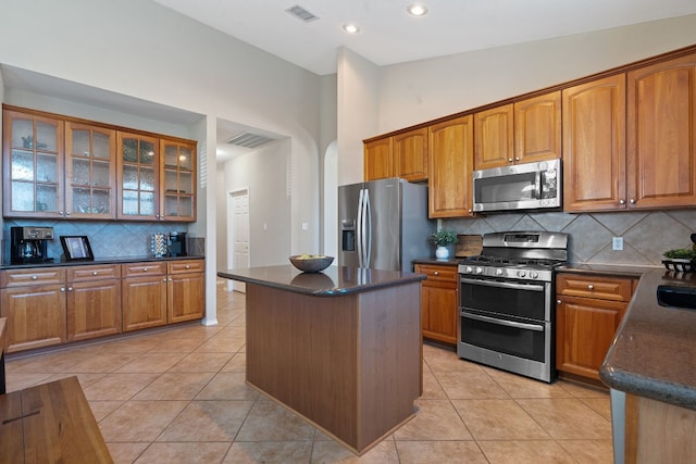 kitchen with stainless steel appliances, light tile patterned flooring, a kitchen island, and decorative backsplash