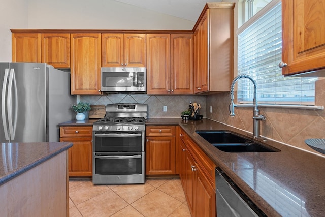 kitchen featuring appliances with stainless steel finishes, lofted ceiling, sink, backsplash, and light tile patterned floors