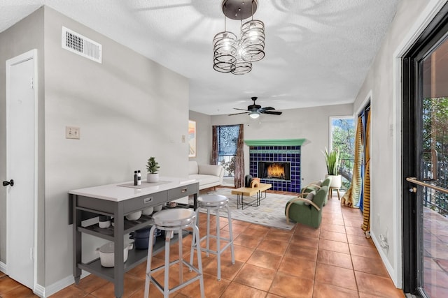 dining room featuring tile patterned flooring, ceiling fan with notable chandelier, a fireplace, and a textured ceiling