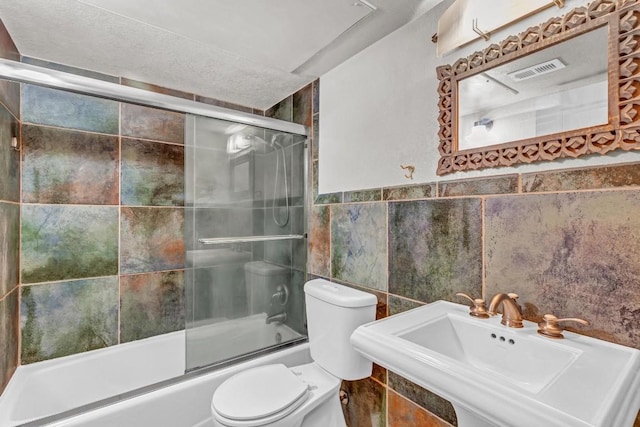 full bathroom featuring bath / shower combo with glass door, sink, tile walls, and toilet