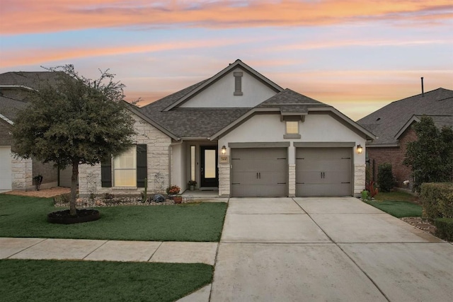 traditional-style home with a garage, stone siding, roof with shingles, a yard, and stucco siding