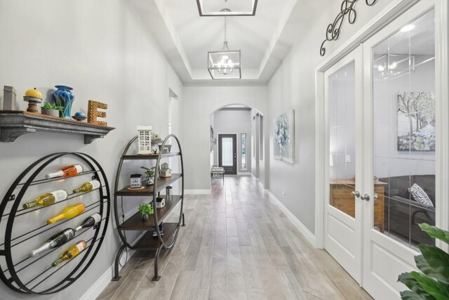 hall featuring french doors, a tray ceiling, a chandelier, and light hardwood / wood-style flooring