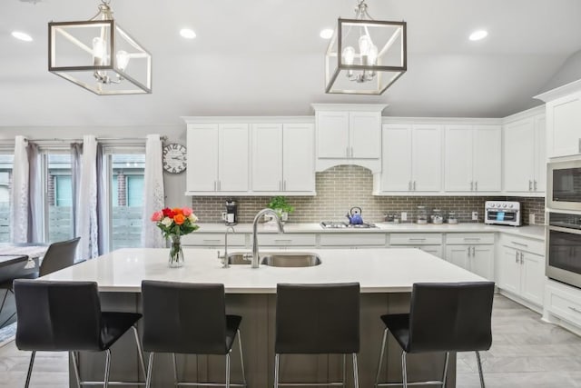 kitchen featuring stainless steel appliances, backsplash, white cabinetry, a sink, and a chandelier