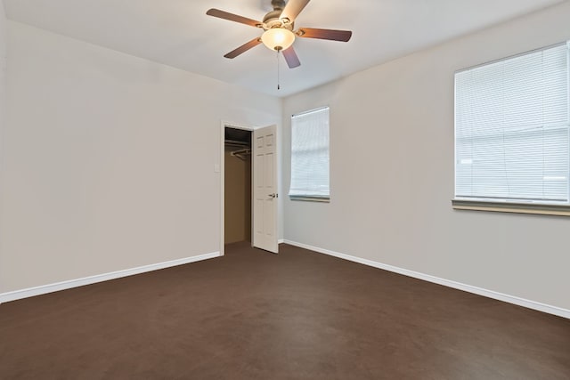 unfurnished bedroom featuring multiple windows, dark colored carpet, ceiling fan, and a closet