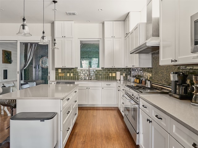 kitchen with white cabinets, decorative light fixtures, wall chimney exhaust hood, and appliances with stainless steel finishes