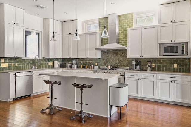 kitchen with white cabinets, a center island, wall chimney exhaust hood, and appliances with stainless steel finishes