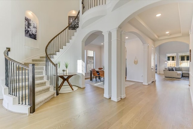 entrance foyer featuring ornate columns, a towering ceiling, and light wood-type flooring