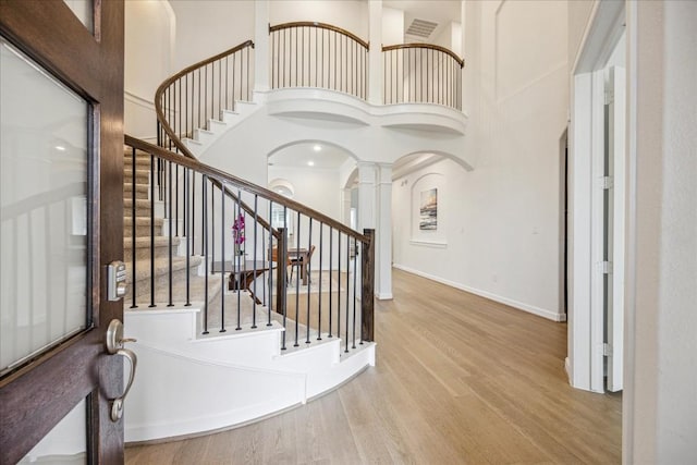 foyer featuring decorative columns, a towering ceiling, and light hardwood / wood-style flooring