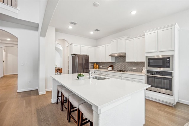 kitchen featuring sink, a breakfast bar area, white cabinetry, stainless steel appliances, and a center island with sink