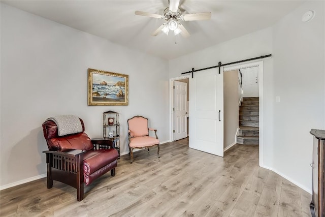 living area with ceiling fan, a barn door, and light hardwood / wood-style floors