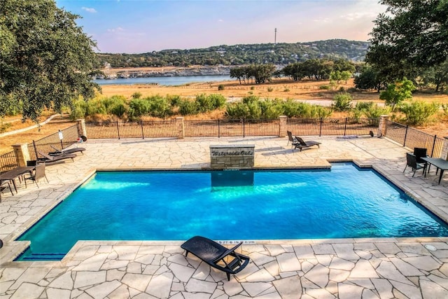 pool at dusk with a water view and a patio area