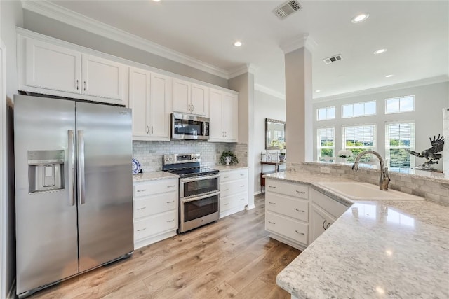 kitchen with sink, white cabinets, stainless steel appliances, crown molding, and light stone countertops