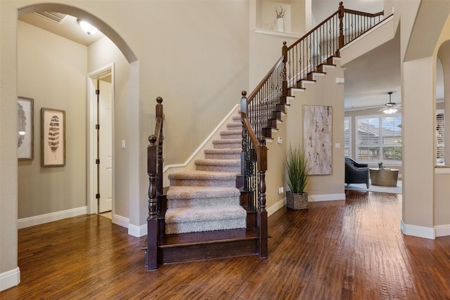 staircase with hardwood / wood-style flooring, a towering ceiling, and ceiling fan