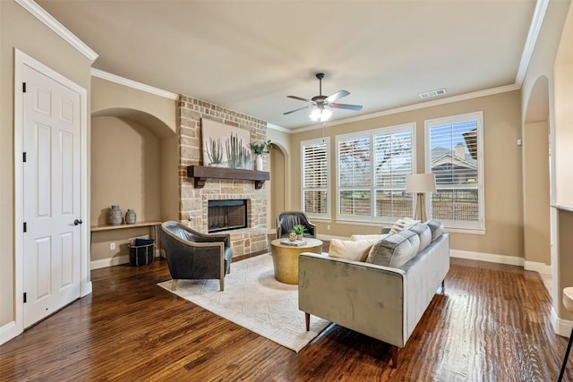 living room featuring dark hardwood / wood-style floors, ceiling fan, ornamental molding, and a stone fireplace