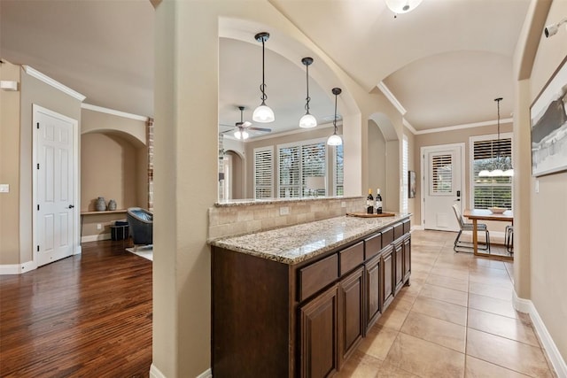 kitchen featuring crown molding, ceiling fan, hanging light fixtures, light stone counters, and tasteful backsplash