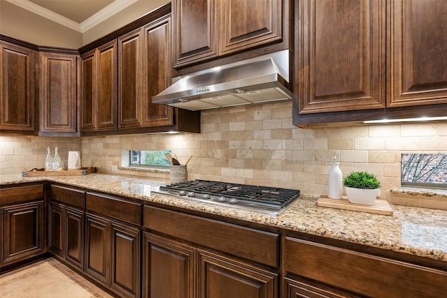 kitchen featuring stainless steel gas stovetop, backsplash, light stone counters, dark brown cabinetry, and crown molding