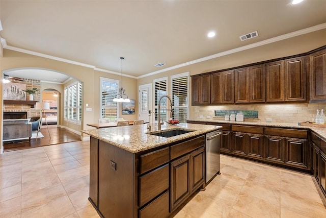 kitchen with sink, light stone counters, an island with sink, pendant lighting, and backsplash