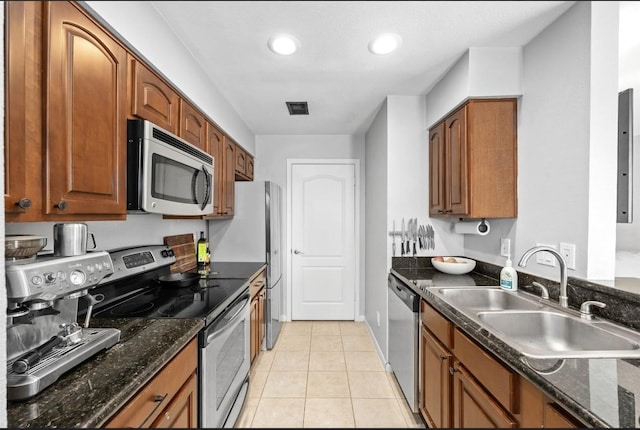 kitchen with dark stone countertops, sink, light tile patterned floors, and appliances with stainless steel finishes