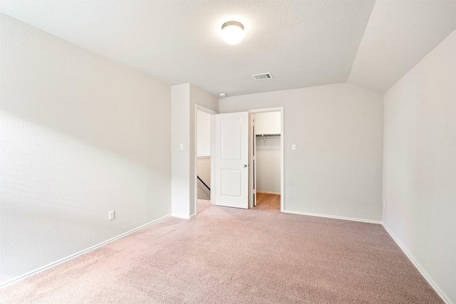 unfurnished bedroom featuring lofted ceiling, a textured ceiling, a spacious closet, light colored carpet, and a closet