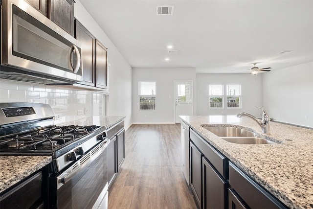 kitchen with light stone counters, dark brown cabinetry, stainless steel appliances, and sink