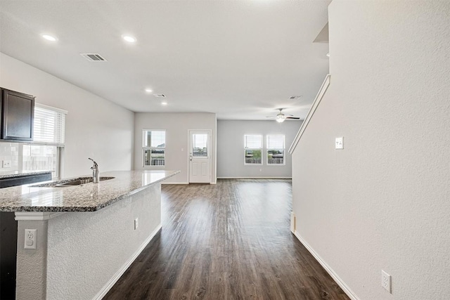 kitchen featuring dark wood-type flooring, sink, a center island with sink, ceiling fan, and light stone countertops