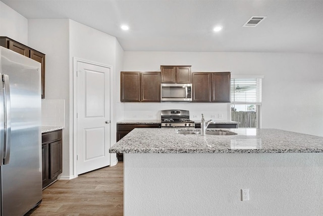 kitchen featuring stainless steel appliances, light stone countertops, a kitchen island with sink, and sink